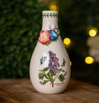 Teardrop-shaped white ceramic vase features design of a purple lilac flanked by butterflies below a three-dimensional accent of other flowers near the top, below a green vine that rings the opening