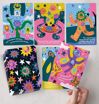 Model's hand holds a card from the Gentle Reminders daily oracle deck above a spread of four others next to the full deck, all with playful, colorful illustrations