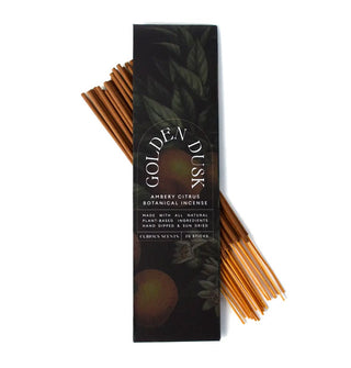 Darkly illustrated rectangular pack of Golden Dusk Ambery Citrus Botanical Incense is placed atop a bundle of 20 sticks