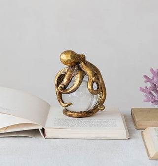 Gold octopus and glass ball figurine rests atop an opened book alongside other books and purple coral