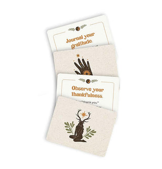 Spread of four Gratitude: A Little Deck of Appreciation cards, two with backs shown featuring hand and stag-headed kneeling woman illustrations, two which say, "Journal your gratitude" and "Observe your thankfulness" respectively