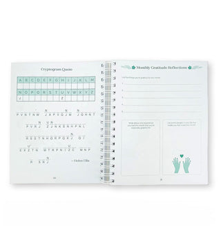 Page spread from spiral-bound Gratitude Puzzle Journal features a Cryptogram Quote puzzle and Monthly Gratitude Reflections section with prompts