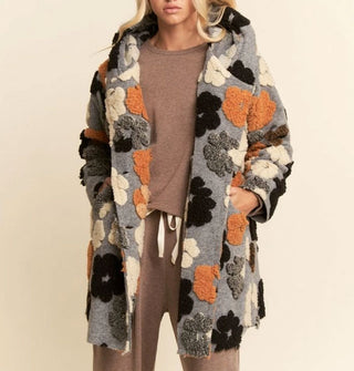Model wears a gray hooded coat with black, gray, orange, and white plush poppy print
