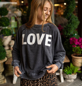 Smiling model wears a dark gray distressed-effect sweatshirt that says, "LOVE" in large white letters
