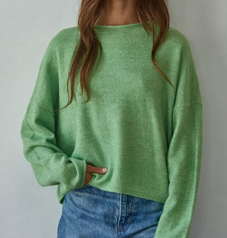 Model wears a slouchy green sweater with rolled boat neckline