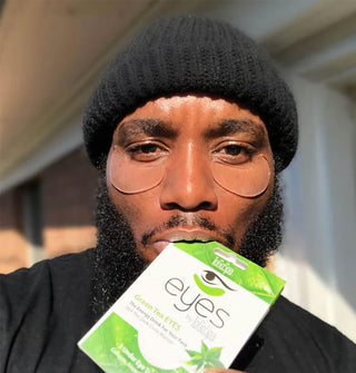Model biting a ToGoSpa Green Tea Eyes mask packet wears the clear patches under eyes