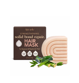 Light peach-colored C-shaped ribbed bar of Kitsch Strengthening Solid Bond Repair Hair Mask sits alongside its brown box packaging with several green bamboo-like plant