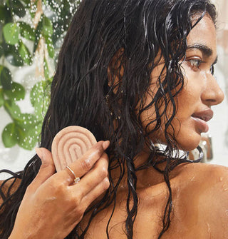 Model holds a bar of treatment mask to lengths of damp hair