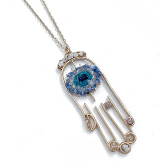 Gold hamsa hand outline necklace pendant with blue and white crystal clusters in the center and others placed at the top, fingertips, and middle finger
