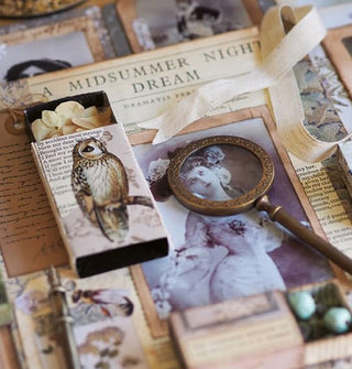 Closeup of a collaged scrapbook page with a brass magnifying glass laying on top of a Victorian woman's face under the caption, "A Midsummer Night's Dream" next to a piece of linen ribbon and a sliding matchbox with owl image