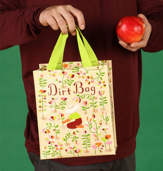 Model holds a "Dirt Bag" gardening tote bag by its handles in one hand and a red apple in the other