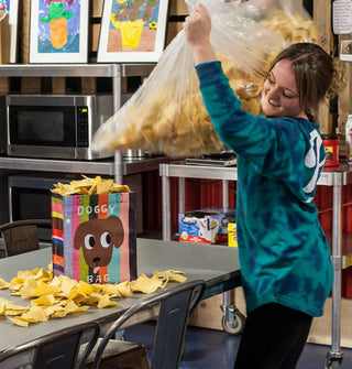 Model dumps tortilla chips from a giant bag into and all around the Doggy Bag tote bag