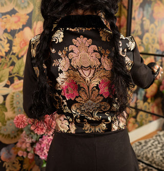 Embroidered metallic floral back panel on a fitted black jacket worn by a model with braided hair