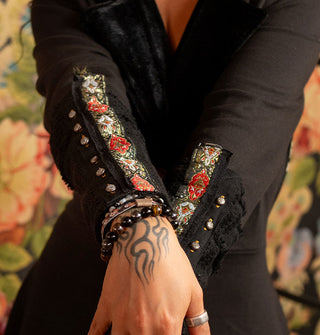 Closeup of floral contrast patches with lace and button trim on the lower half of black jacket sleeves