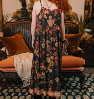 Model facing away from the camera wears a dark sleeveless full-length dress with lush floral print and a banner with text along the bottom hem