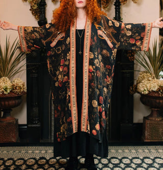 Model with arms outstretched wears a long open-front robe with dark floral print accented with banner graphics and border that says, "Friendship, Love & Truth"