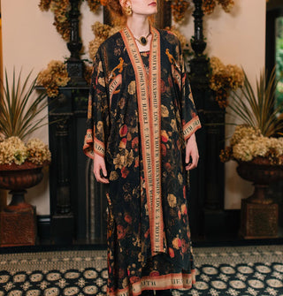 Model wears a long open-front robe with dark floral print accented with banner graphics and border that says, "Friendship, Love & Truth"
