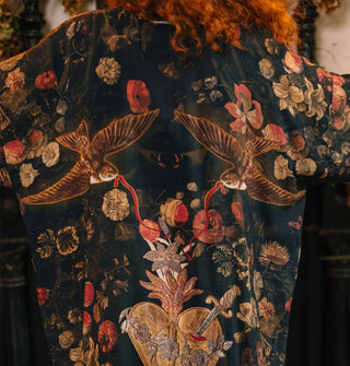 Back of a dark robe with floral print and a design of two swallows holding red ribbon in their beaks above a heart pierced by a dagger