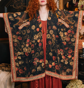 Model with arms outstretched wears a black robe with floral print and contrasting border that says, "Friendship, Love & Truth"