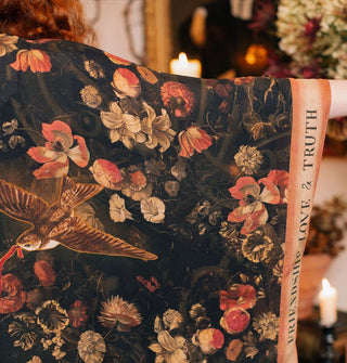 Model wears a black robe with floral print, swallow with red ribbon in its beak, and contrasting border that says, "Friendship, Love & Truth"