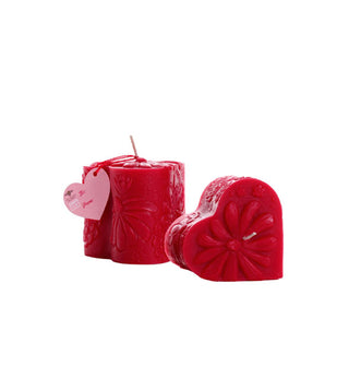 Red heart-shaped mini pillar candles with raised flower designs over their surfaces and a pink heart-shaped tag hanging from the wick of one