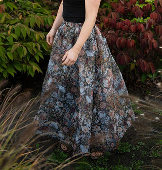 Model standing among lush greenery wears a long, full, floral print skirt