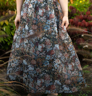 Model standing among lush greenery wears a long, full, floral print skirt