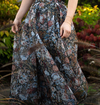 Model standing among lush greenery wears a long, full, floral print skirt