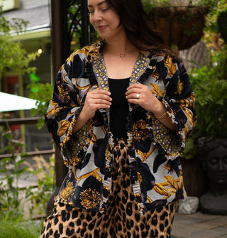 Model holds the lapels of an ornately floral patterned jacket with densely pleated and ruffled edges and a contrasting print lining