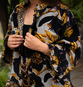 Model holds the lapels of an ornately floral patterned jacket with densely pleated and ruffled edges and a contrasting print lining