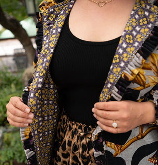 Model holds the lapels of an ornately floral patterned jacket with densely pleated and ruffled edges and a contrasting print lining