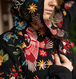 Model wears a black hooded cardigan with colorful embroidered bird and flower designs all over it
