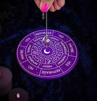 Model's hand holds a crystal pendulum over its accompanying round purple board with white lettering to indicate its answers