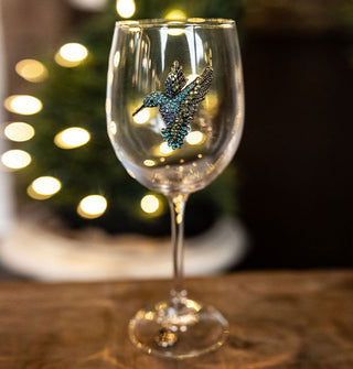 Clear wine glass features a blue bejeweled hummingbird adornment on its bowl