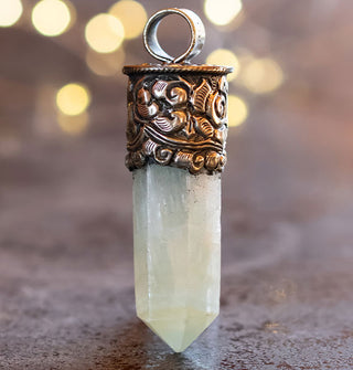 Greenish translucent crystal point in engraved silver pendant setting with rounded top bail