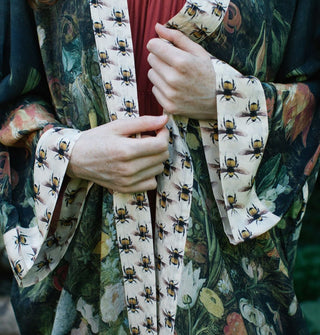 Model wears a kimono-style robe with floral motif and contrasting bee print borders and sleeve cuffs