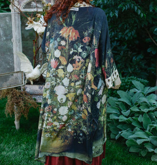 Model facing away from the camera wears a long, kimono-style robe with a lush floral motif and contrasting bee print neckline and sleeve cuff