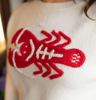 Closeup of an embroidered red and white lobster design on a cream-colored sweater