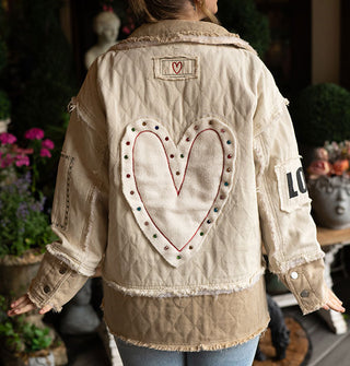 Model facing away from the camera wears a quilted beige and white patchwork jacket with raw seams and a large heart-shaped patch on the back with stud accents