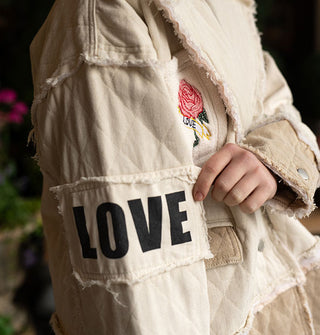 Model wears a quilted beige and white patchwork jacket with raw seams and "Love" patches on the sleeve and chest