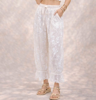 Model wears white pantaloons with flocked velvet floral pattern, elasticated tie waist, and lace trim