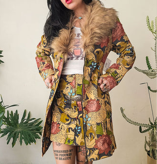 Model wears a long jacket with zipper and fur collar and a mini skirt, both with the same print of cheetahs and flowers