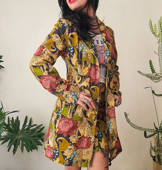 Model wears a long collared jacket with zipper front and a mini skirt, both with the same print of cheetahs and flowers