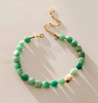 Necklace with gold clasp and extender chain is strung with polished green jade stones and one brown and white accent stone