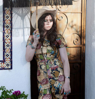 Model holding a fringed parasol wears a jumpsuit with front zipper and print of cheetahs and flowers