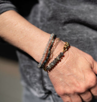 Model wears a bracelet made up of faceted rounded labradorite stones on a chunky brass curb chain with lobster claw clasp