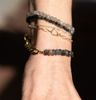 Model wears a bracelet made up of faceted rounded labradorite stones on a chunky brass curb chain