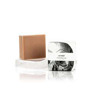 Bar of brown soap alongside its "La Nuit" packaging which features a partially visible black and white illustration of a skull