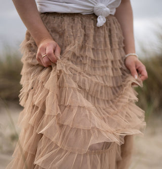 Model's hands clutch the ruffles of a tiered beige tulle skirt