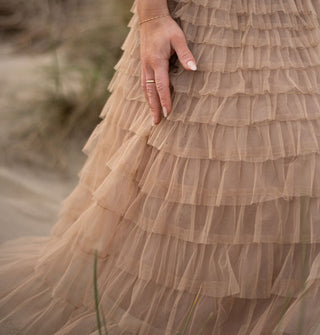 Model's hand rests against the tiered ruffles of a long tulle skirt